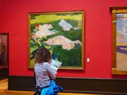 Uma mulhar lendo um folheto em frente a uma obra de Sorolla