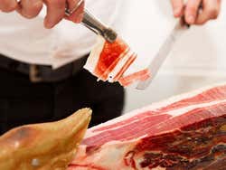 Detalhe de uma pessoa cortando pedaços de jamón